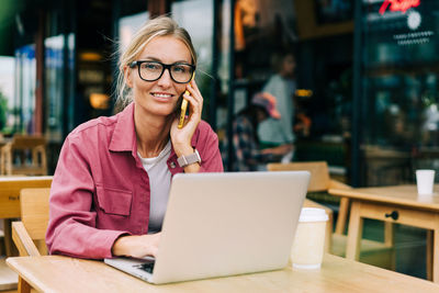 Young attractive business woman in glasses sitting at a table in a cafe working on a laptop.