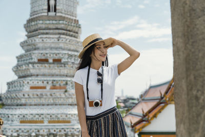 Woman wearing hat standing against built structure