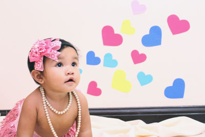 Shirtless baby girl looking away while kneeling on bed at home