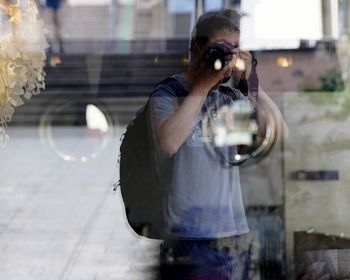 Reflection of man photographing in city