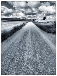 Road passing through field against cloudy sky