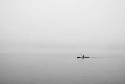 Person on boat in sea against clear sky during foggy weather