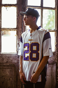 Young man looking away while standing against window