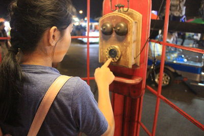 Rear view of woman dialing on rotary phone in booth at night