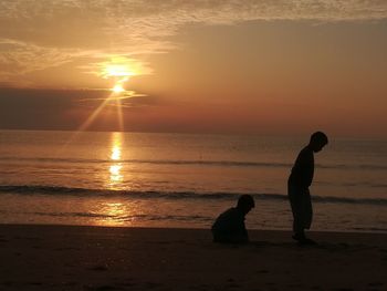 Silhouette people on beach against sky during sunset