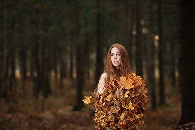 Portrait of woman standing by tree in forest