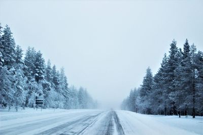 Winter road amidst trees against white sky
