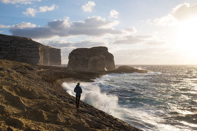 Man standing on rock by sea against sky