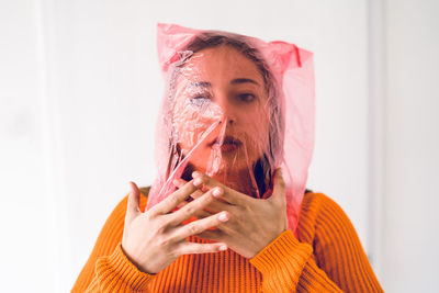 Portrait of teenage girl face covered with plastic bag standing against wall at home