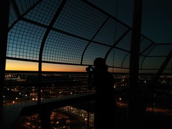 Silhouette woman standing by suspension bridge in city at night