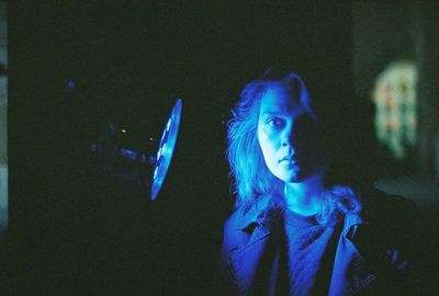 Portrait of young woman standing by blue illuminated light in darkroom