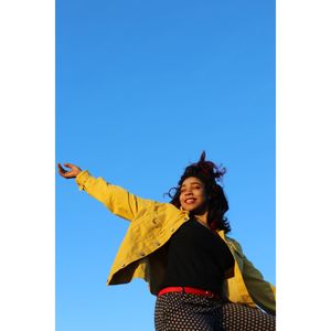 Low angle view of young woman with arms outstretched standing against clear blue sky