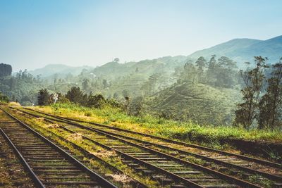 Railroad tracks by trees and mountains against sky