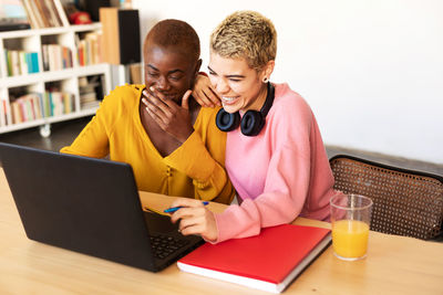 Cheerful lesbian couple using laptop on table at home