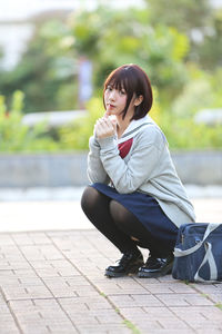 Young woman in school uniform crouching at park