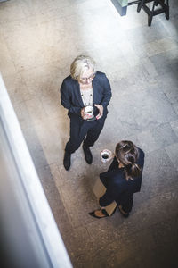 High angle view of female colleagues drinking coffee while standing in office
