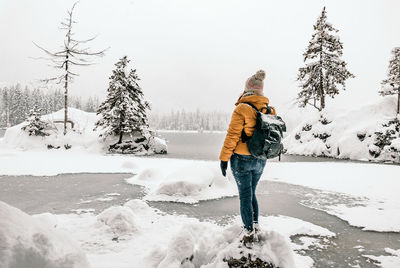 Rear view of person in winter clothes standing on shore of frozen lake.