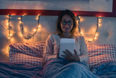 Young woman using digital tablet while sitting on bed at home