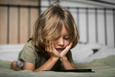 Boy lying on the bed using digital tablet computer playing games or watching cartoons at home.