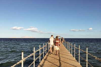 Rear view of couple walking on pier over sea against sky