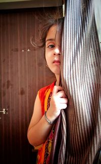 Cute girl looking away while standing against curtain