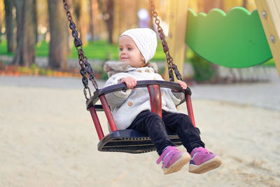 Cheerful cute girl sitting on swing at playground