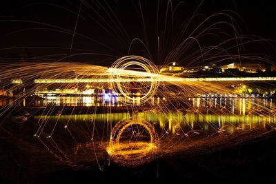 Light trails in river against sky at night