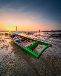 Boat moored on beach against sky during sunset
