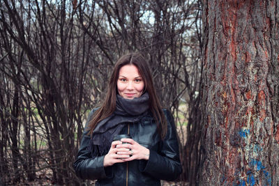 Portrait of smiling young woman wearing warm clothing against bare trees