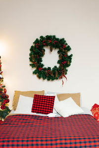 A christmas wreath hangs over the bed with a red plaid blanket in the bedroom