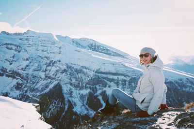Woman sitting on snow covered mountain against sky
