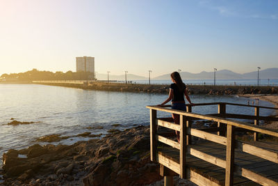 Woman standing by railing and sea against sky