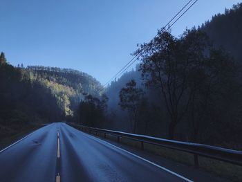 Scenic view of empty road along trees against clear blue sky