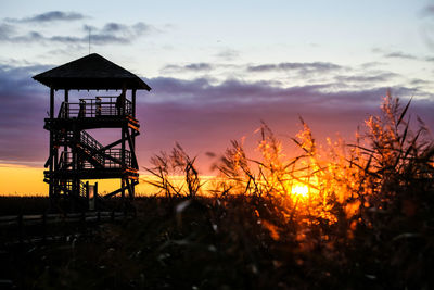Silhouette tower on field against sky during sunset