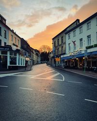 Road by buildings against sky during sunset in city