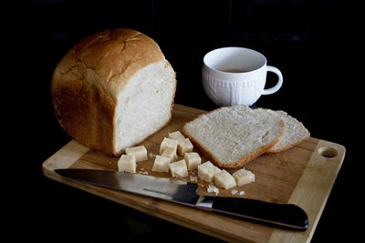 Bread and knife on cutting board by coffee cup over black background