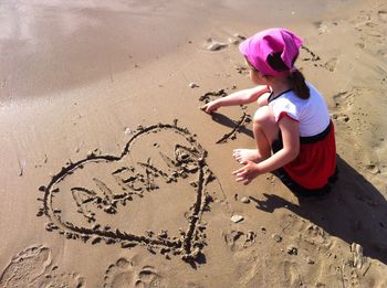 High angle view of girl writing in sand on shore at beach during summer