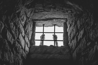 Low angle view of man holding window bars from inside historic building