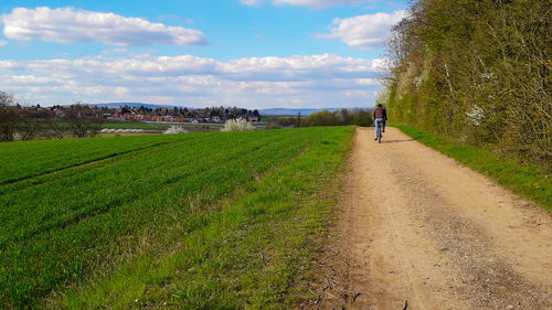 Man walking on road amidst field against sky