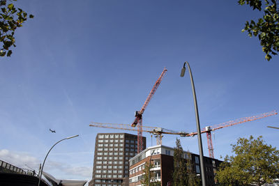 Low angle view of crane by building against sky