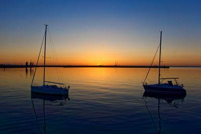 Sailboats moored in marina at sunset