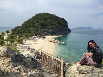 Cheerful woman sitting on rock by sea against sky