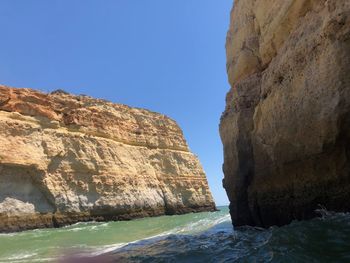 Rock formations by sea against clear blue sky