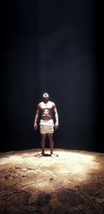 Full length of shirtless young man standing against black background