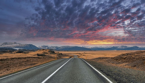 Empty vanishing road amidst volcanic landscape against cloudy sky during sunset