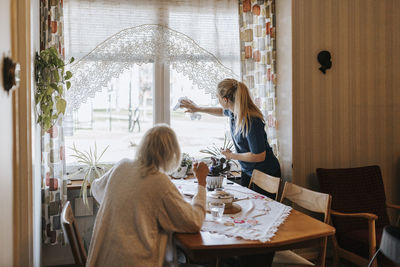 Senior woman looking at female caregiver cleaning window glass at home