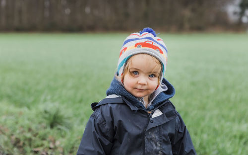 Portrait of cute baby girl in warm clothing standing on grassy field