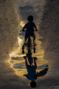 Rear view of people on sea shore against sky during sunset