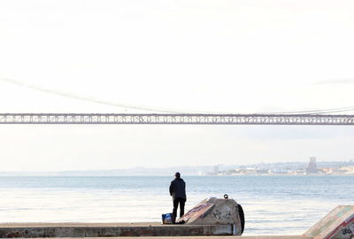 Rear view of man standing on bridge over sea against clear sky