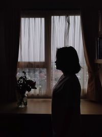 Side view of woman by window at home